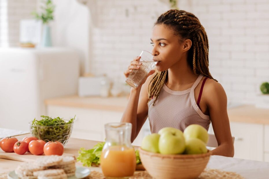 woman drinking water in front of several fruits